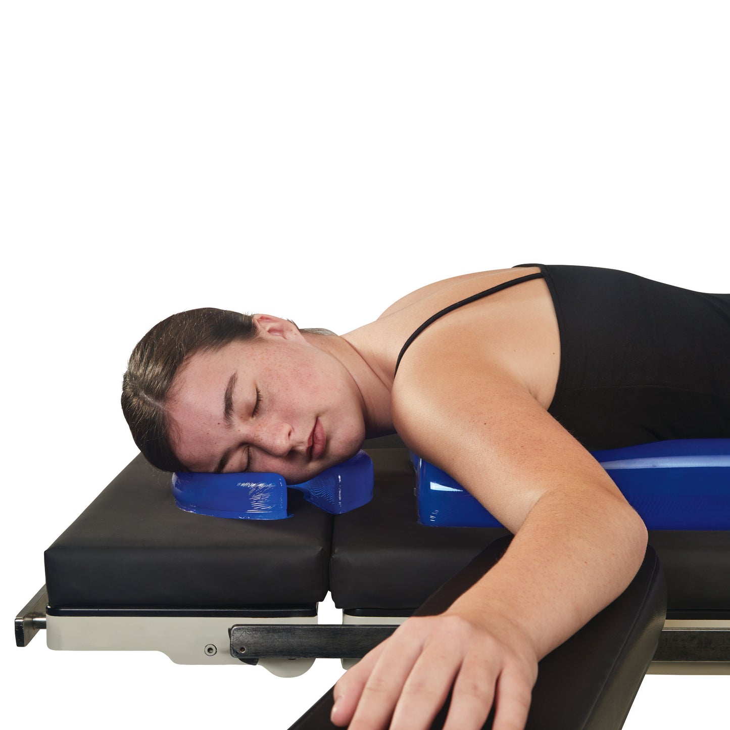 A woman lies face down on a black surface, using the AliMed AliBlue Gel Horseshoe Donut as a headrest.