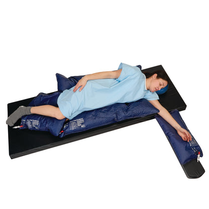 A person lies on a black mattress using the AliMed Bean Bag Positioner with Cutout. They wear a blue gown and gray socks.