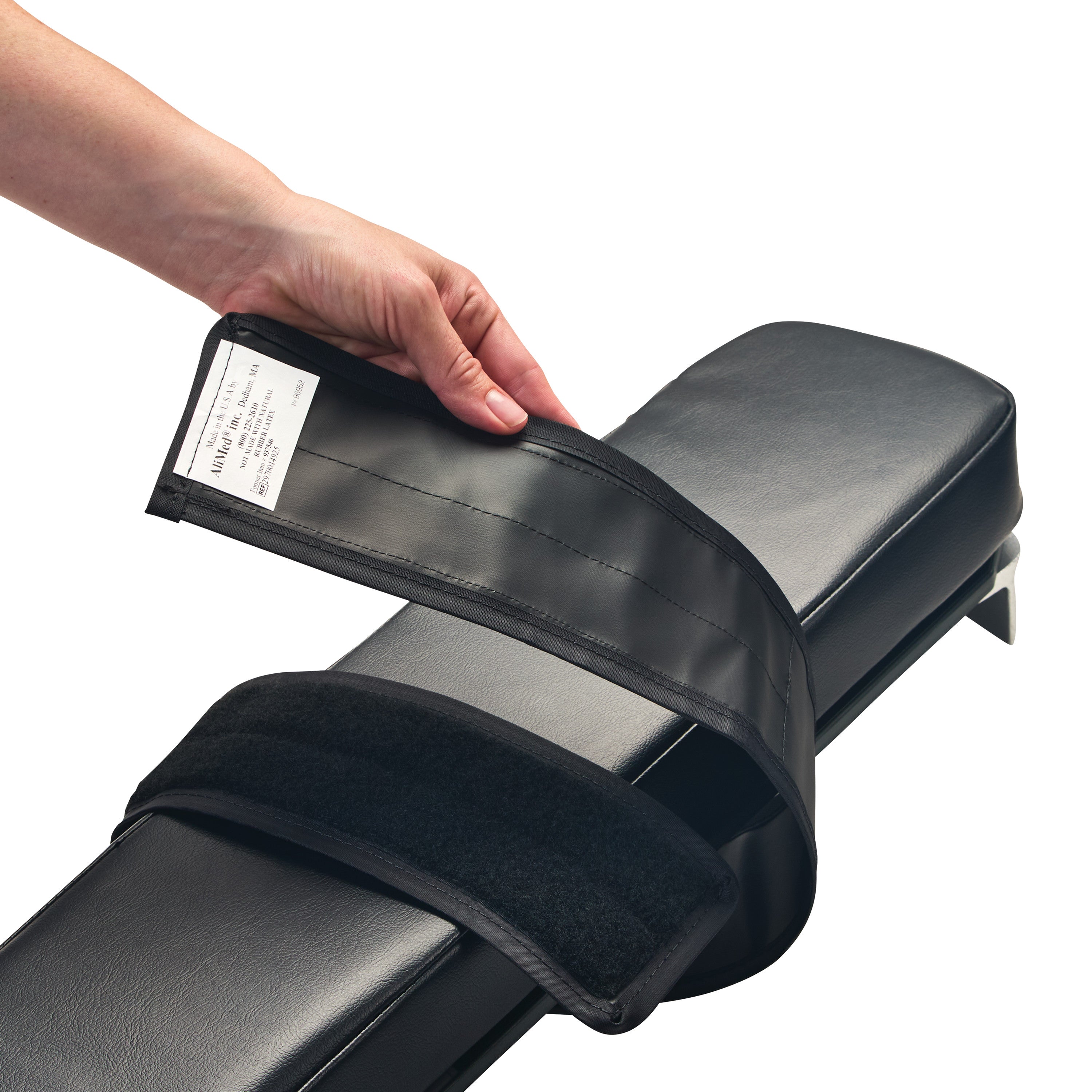 A hand holds the AliMed Reusable Armboard Strap over a black padded armboard, showing the adjustable Velcro strap design.