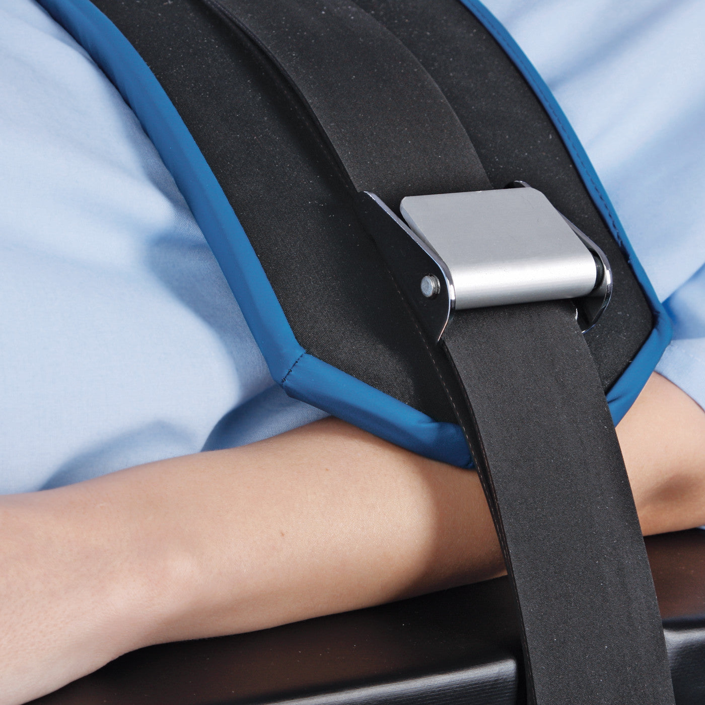 An AliMed Deluxe Padded O.R. Table Strap securing a person's arm. The strap is black with a silver buckle and blue padding.