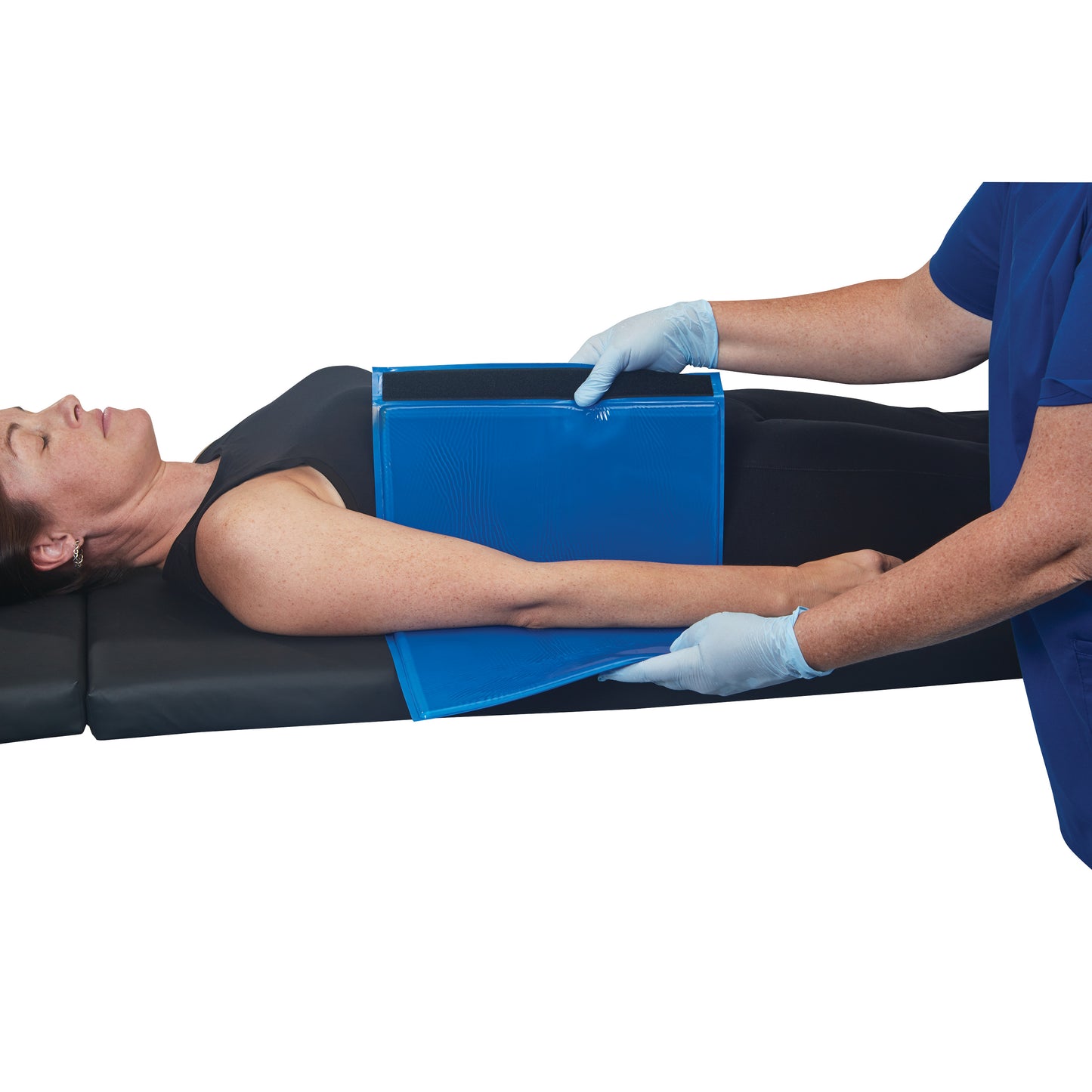 A person lies on their back with an AliMed AliBlue Gel Ulnar Forearm Protector placed under their forearm, held by gloved hands.