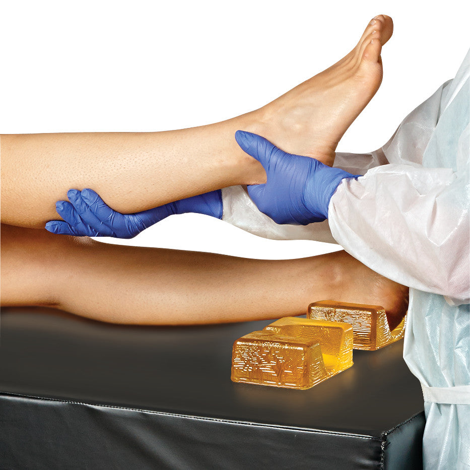 A medical professional in gloves positions a patient's leg using the AliMed AliGel Basic Positioning Set on a black surface.