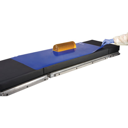 An AliMed Nonslip Surface Overlay on a medical table, featuring a blue mat with a yellow cushion on top.