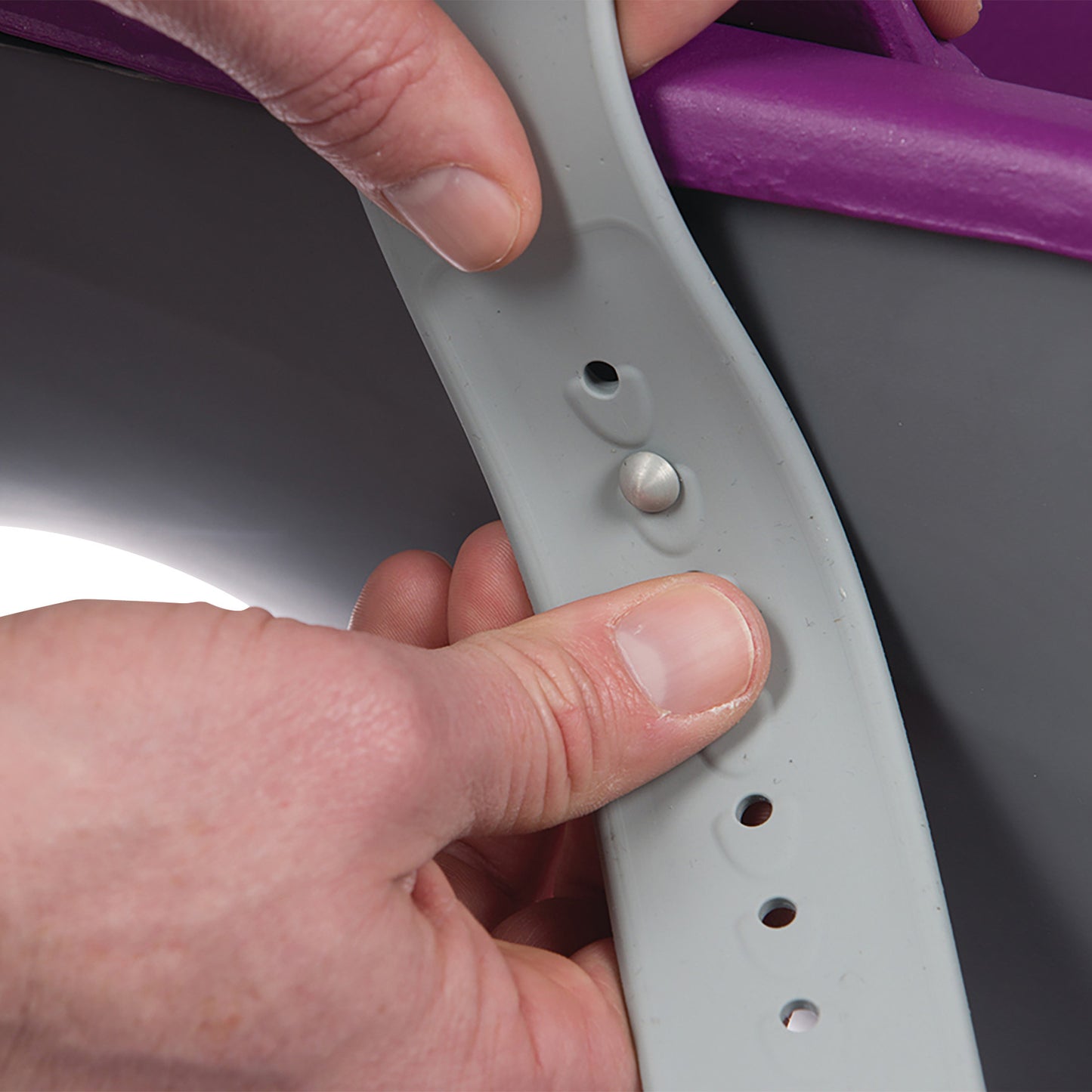 Hands adjust the gray strap of a KYRA Clean 350 Lithotomy Stirrup with multiple holes and a metal peg for fastening.