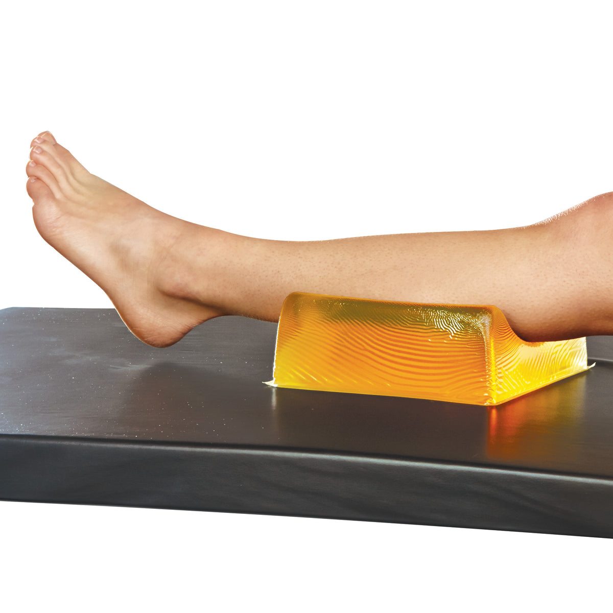 A leg rests on an AliMed AliGel Contoured Head Rest placed on a black surface, showing its use for support or positioning.