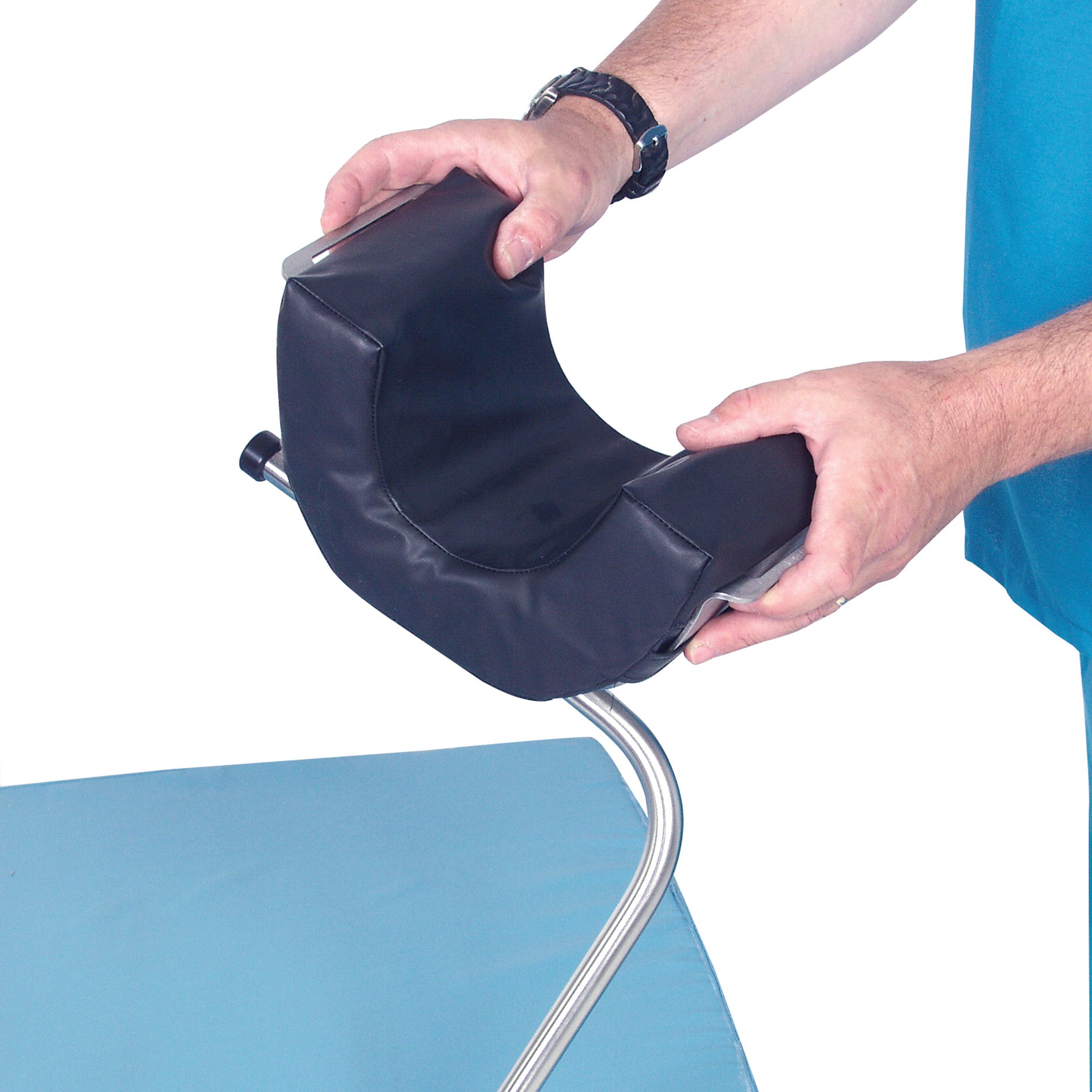 A person holds the AliMed Standard Universal Positioner, a cushioned, U-shaped support with a metal frame, above a blue surface.