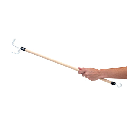 A hand holds a "Big Hook Dressing Stick" with a wooden handle and metal hooks on both ends against a white background.
