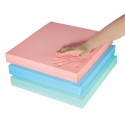 A hand presses a pink AliMed T-Foam Uncovered Wheelchair Cushion stacked on blue and teal cushions, leaving an imprint.