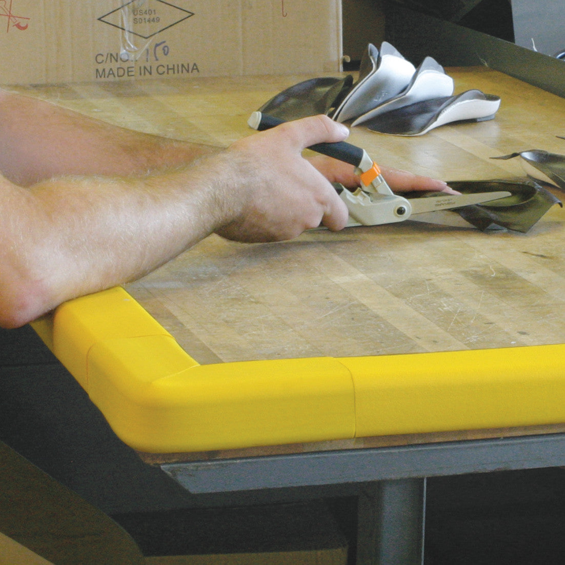 A person works at a table with AliMed SoftEdge Corner Protector, which has a yellow padded edge for safety.
