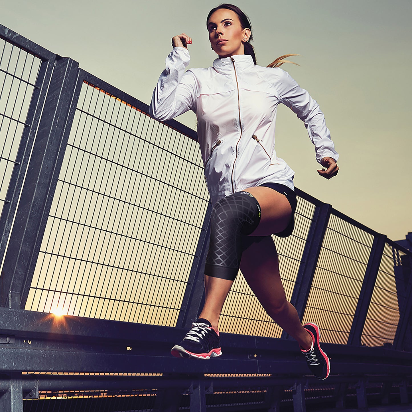 A person is running while wearing a Brownmed Spark Kinetic Knee Sleeve on their left knee, along with athletic gear and shoes.