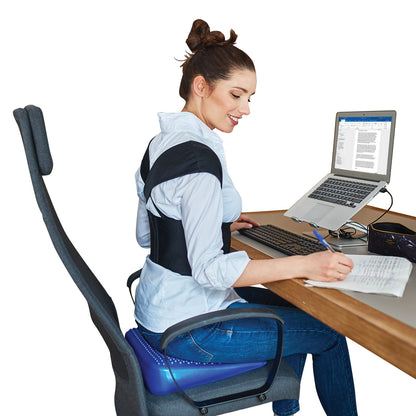 A woman uses a laptop at a desk while wearing the Femi Posture brace. She is sitting on a cushion with a supportive chair back.