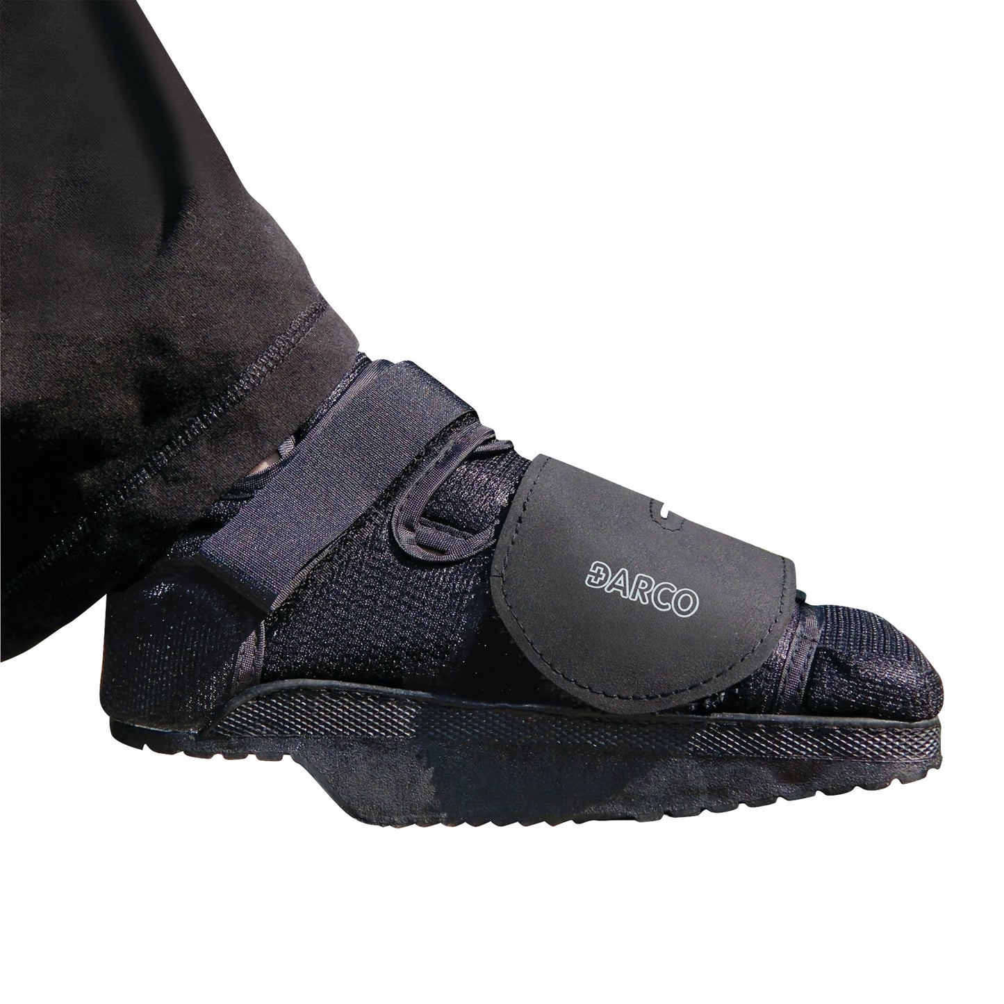 A person wears a DARCO HeelWedge Healing Shoe with a black upper, straps, and a wedge sole designed for post-surgery recovery.