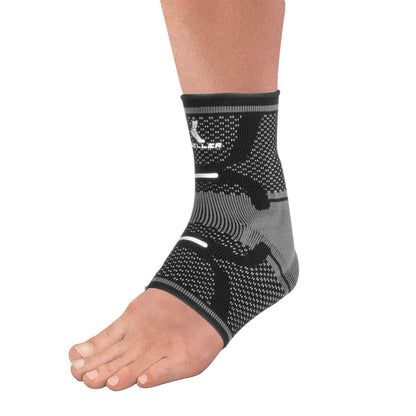 A foot wearing a Mueller Omniforce Ankle Support, a black and gray compression sleeve providing support and stability to the ankle.