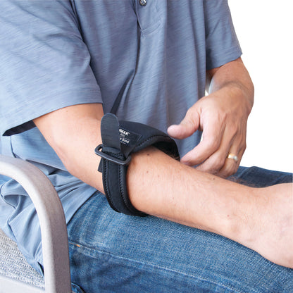 A person adjusts a Brownmed IMAK RSI Elbow Band on their forearm while sitting. The band is black with hook and loop closure