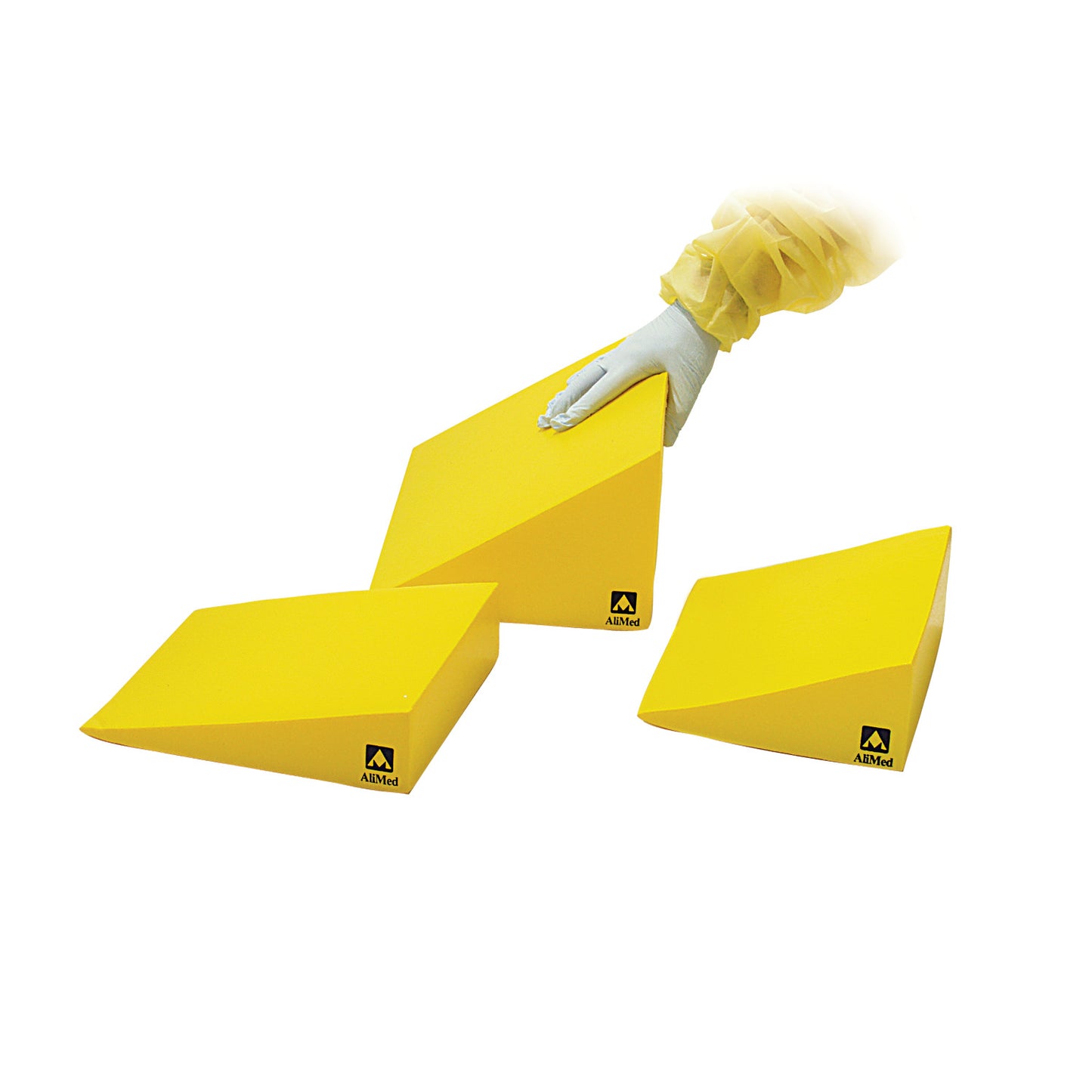 A person wearing gloves adjusts a yellow AliMed Protecta-Coat 15 Degree Wedge Positioner, with two additional wedges nearby.