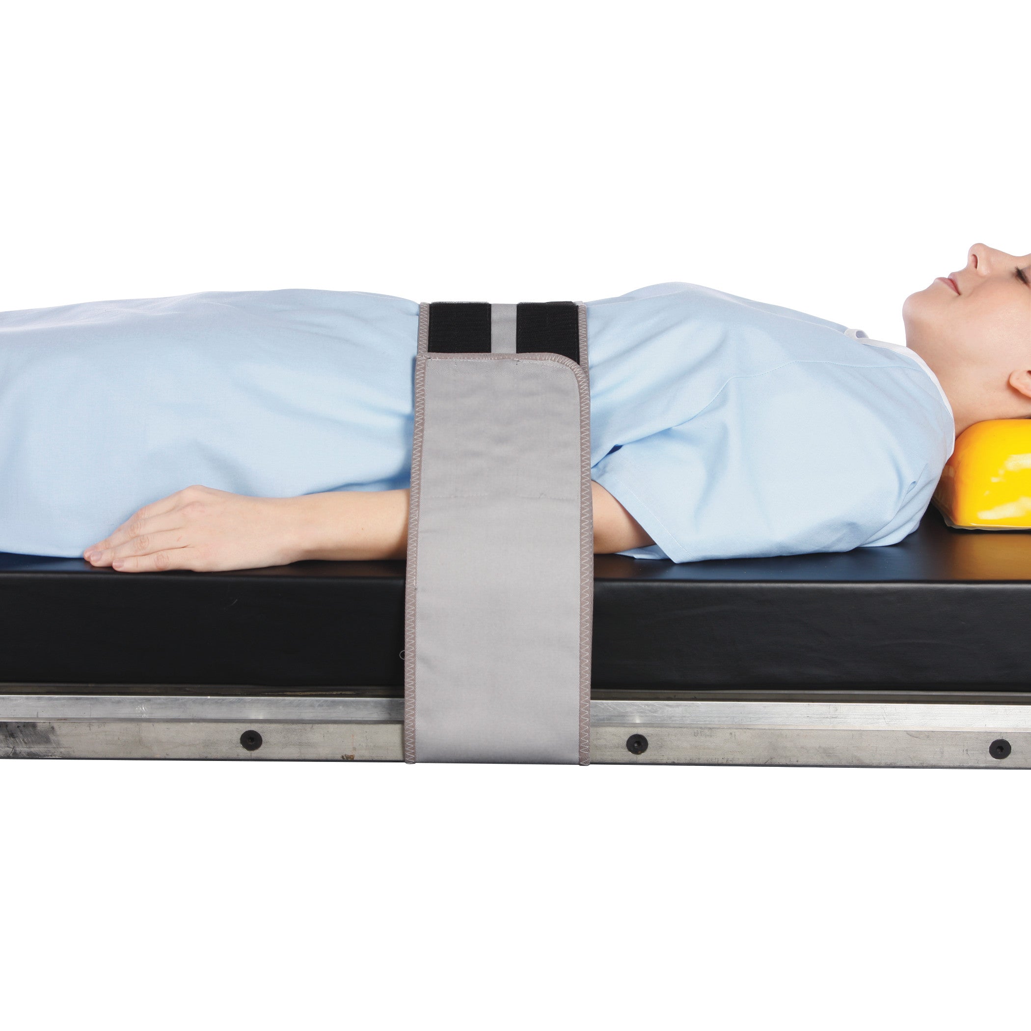 A person lies on a table secured with the AliMed Universal Body Strap, with arms at their sides and a yellow headrest.