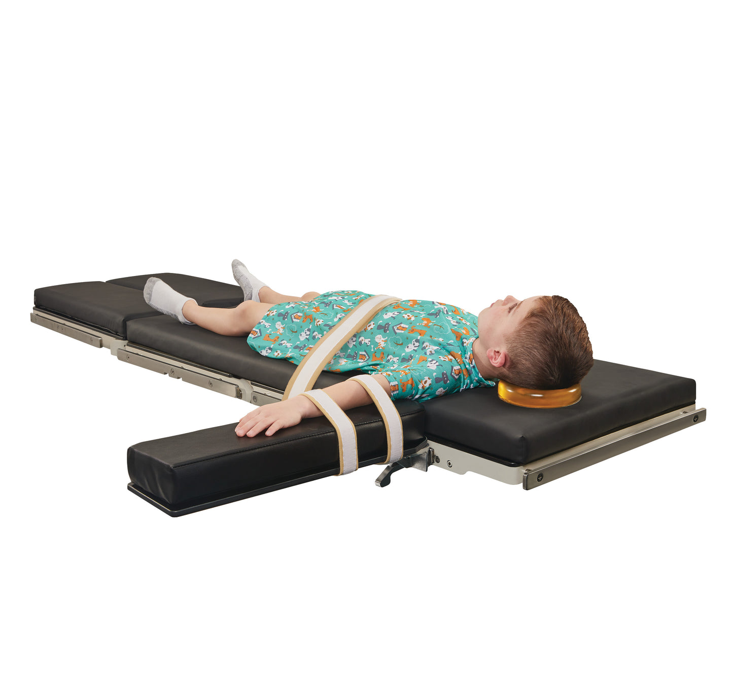 A child is secured on a padded medical table using AliMed AliStrap Soft Positioning Straps. The child is wearing a patterned gown.