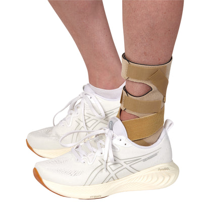 A person wears the AliMed FREEDOM Soft Footdrop Brace with white sneakers. The brace supports the ankle with tan straps.