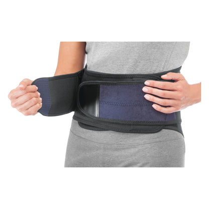 A person adjusts the Mueller Adjustable Back Brace around their waist, showing its black and blue design and strap closure.