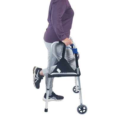 A person using a walker with their knee supported by the SafetySure The Knee Sling, wearing a purple top, gray pants, and black sneakers.