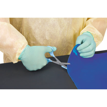 Person wearing gloves and a gown cuts the AliMed Nonslip Surface Overlay, a blue sheet, with scissors on a black surface.