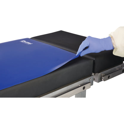 A gloved hand lifts a corner of the AliMed Nonslip Surface Overlay, which is blue and placed on a black medical table.