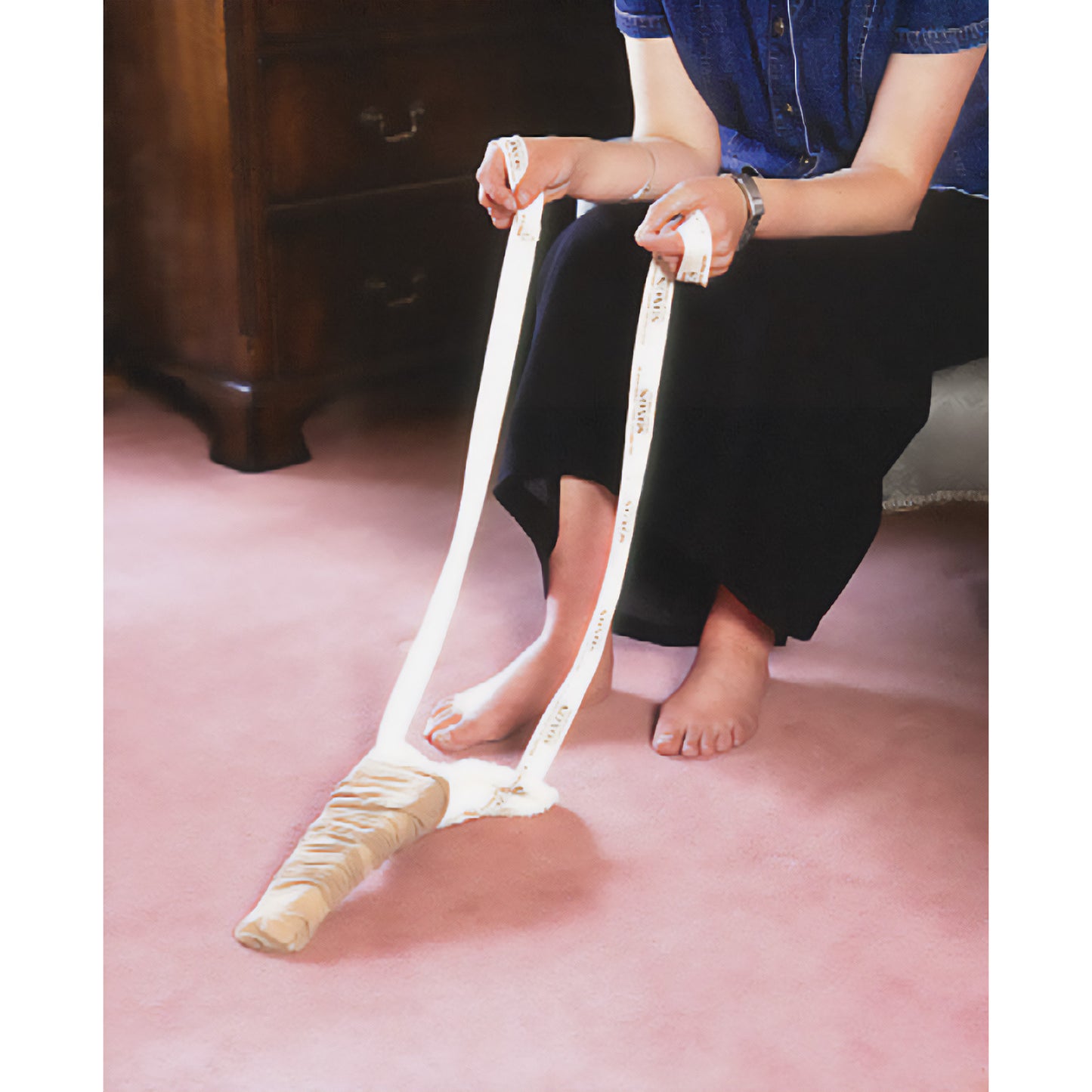 A person uses the Soxon Terrycloth Sock Aid on a carpeted floor, helping to put on socks without bending over.