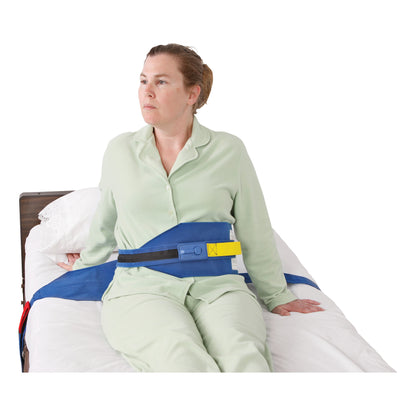 A person sits on a bed wearing an AliMed Roll-Control Belt, a blue safety restraint with a yellow and black buckle.