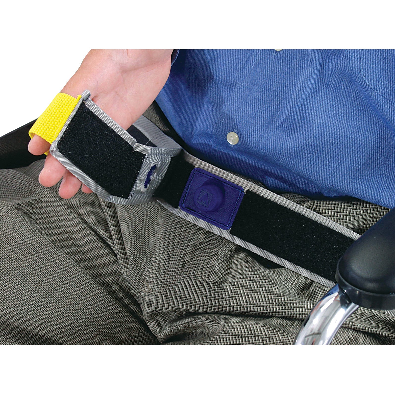 A person holds the AliMed E-Z Release Seatbelt with Basic Alarm, featuring a hook-and-loop fastener, against gray pants and a blue shirt.