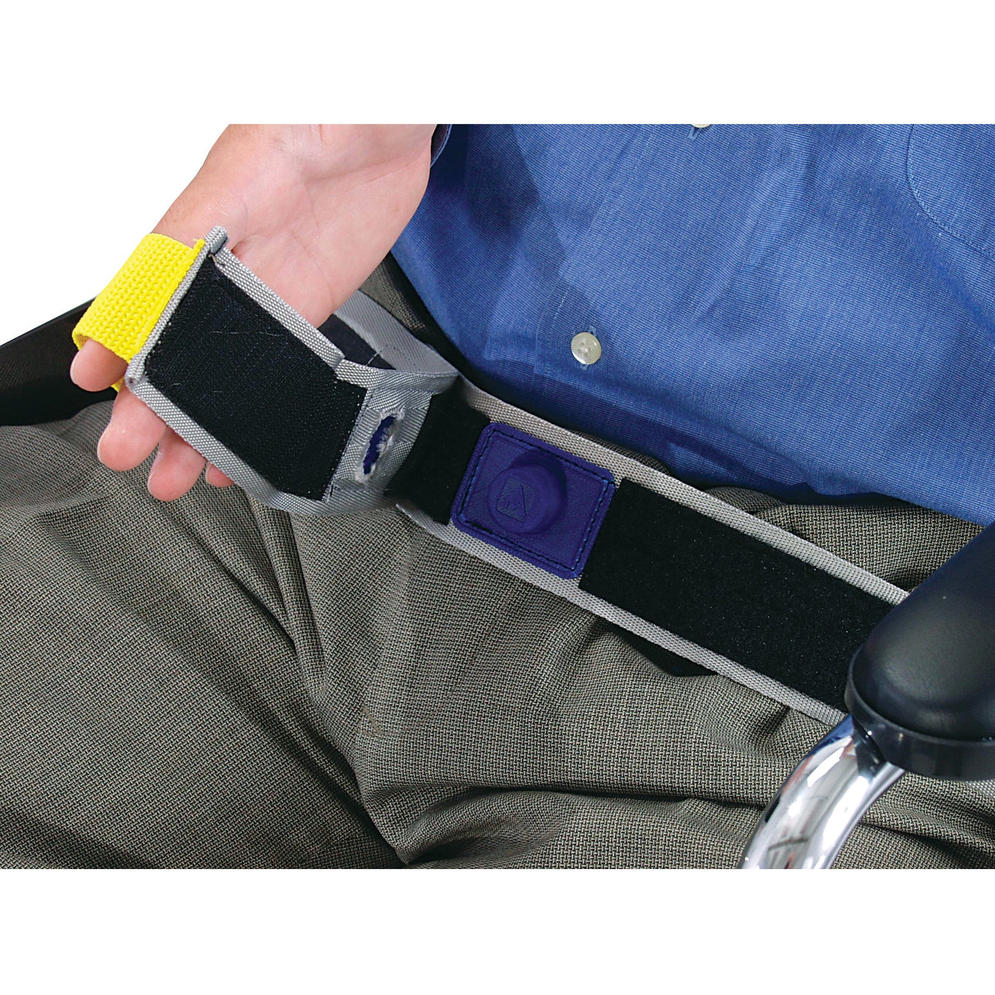 A person holds the AliMed E-Z Release Seatbelt with Basic Alarm, featuring a hook-and-loop fastener, against gray pants and a blue shirt.
