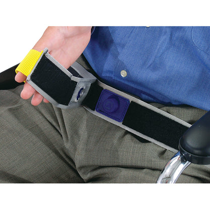 A person holds the AliMed E-Z Release Seatbelt with Basic Alarm, featuring a hook-and-loop fastener, against gray pants and a blue shirt.
