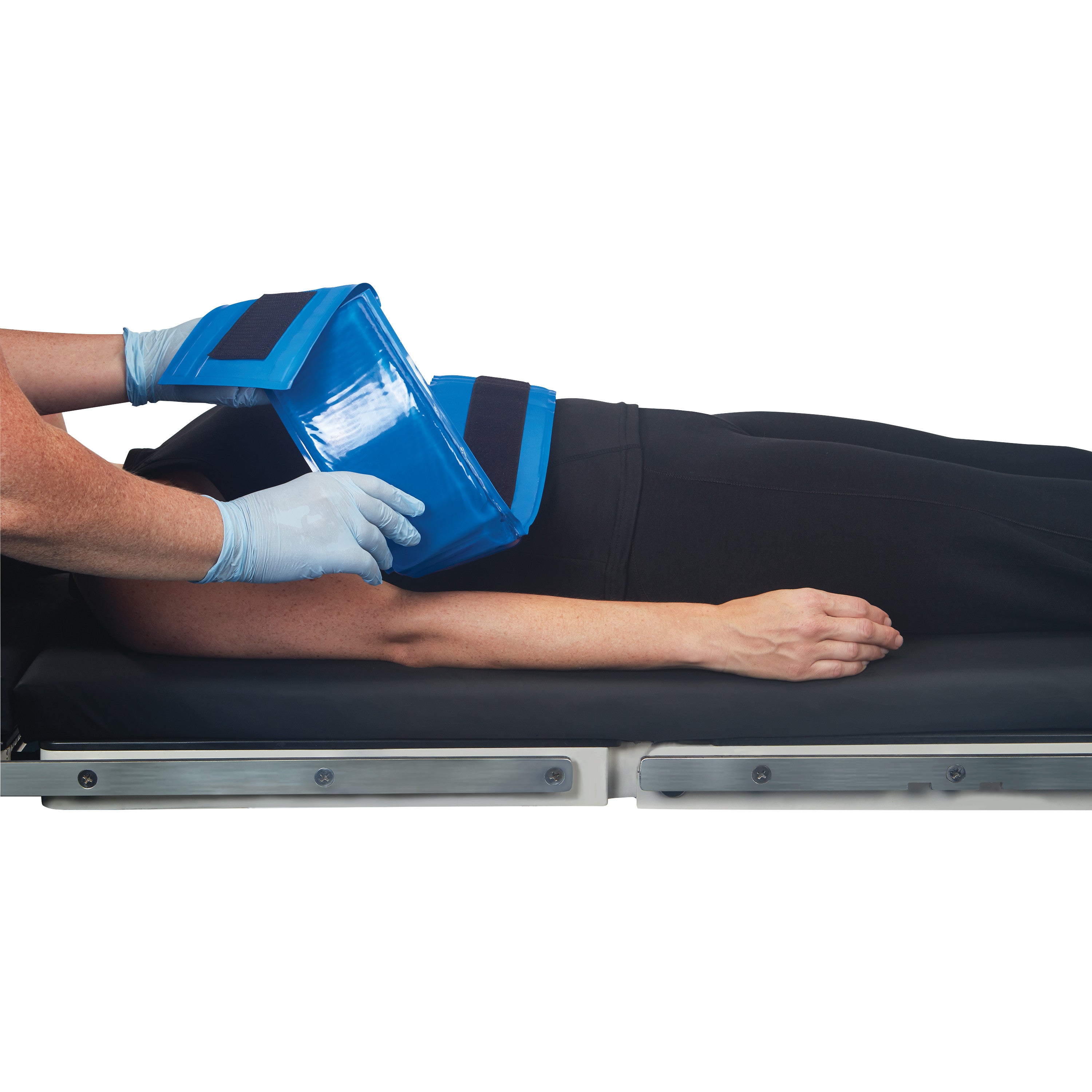 A person with gloved hands applies an AliMed AliBlue Gel Body Strap to a patient's arm on a medical examination table.