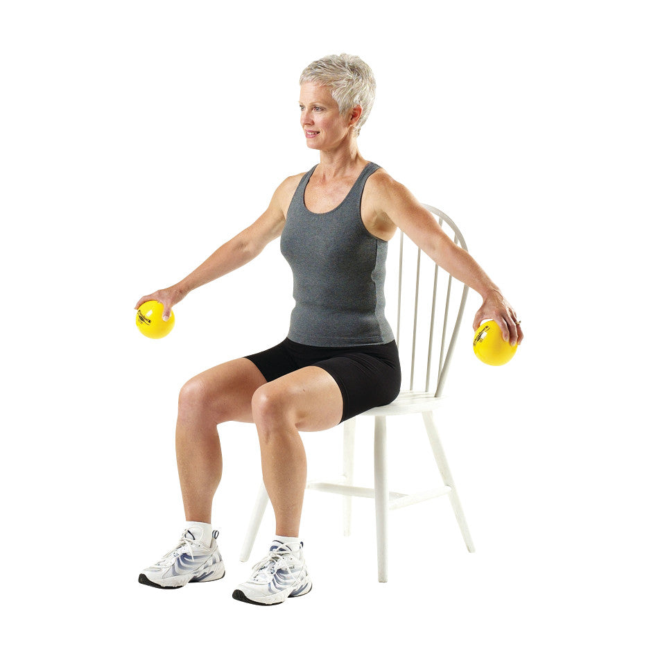 A person sits on a chair, holding yellow THERABAND Soft Weights, exercising with arms extended outward.