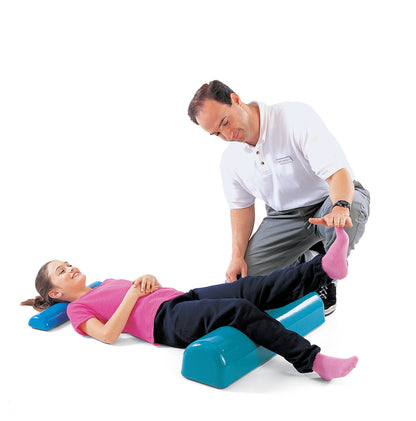 A child lies on a Tumble Forms2 Half Roll while an adult assists with leg exercises. The half roll is blue.
