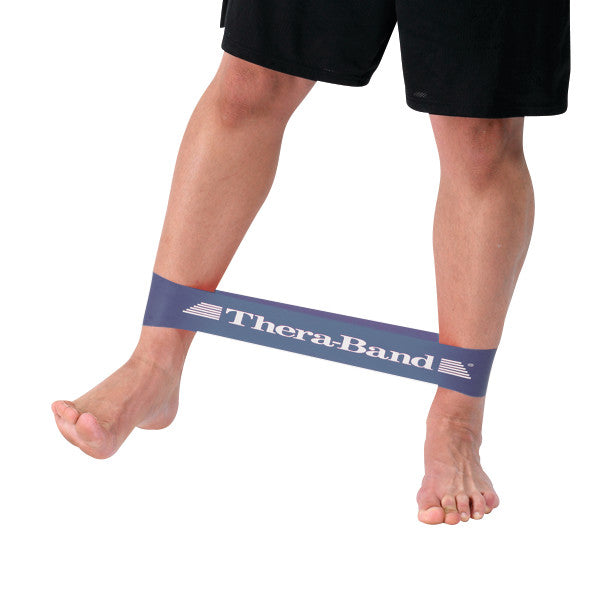 A person exercises with a THERABAND Resistance Band Loop around their ankles, stretching one leg sideways.