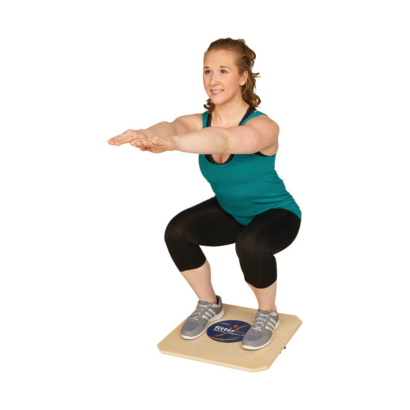 A person squats on a Fitterfirst Professional Balance Board, wearing athletic apparel, illustrating its use for balance training.