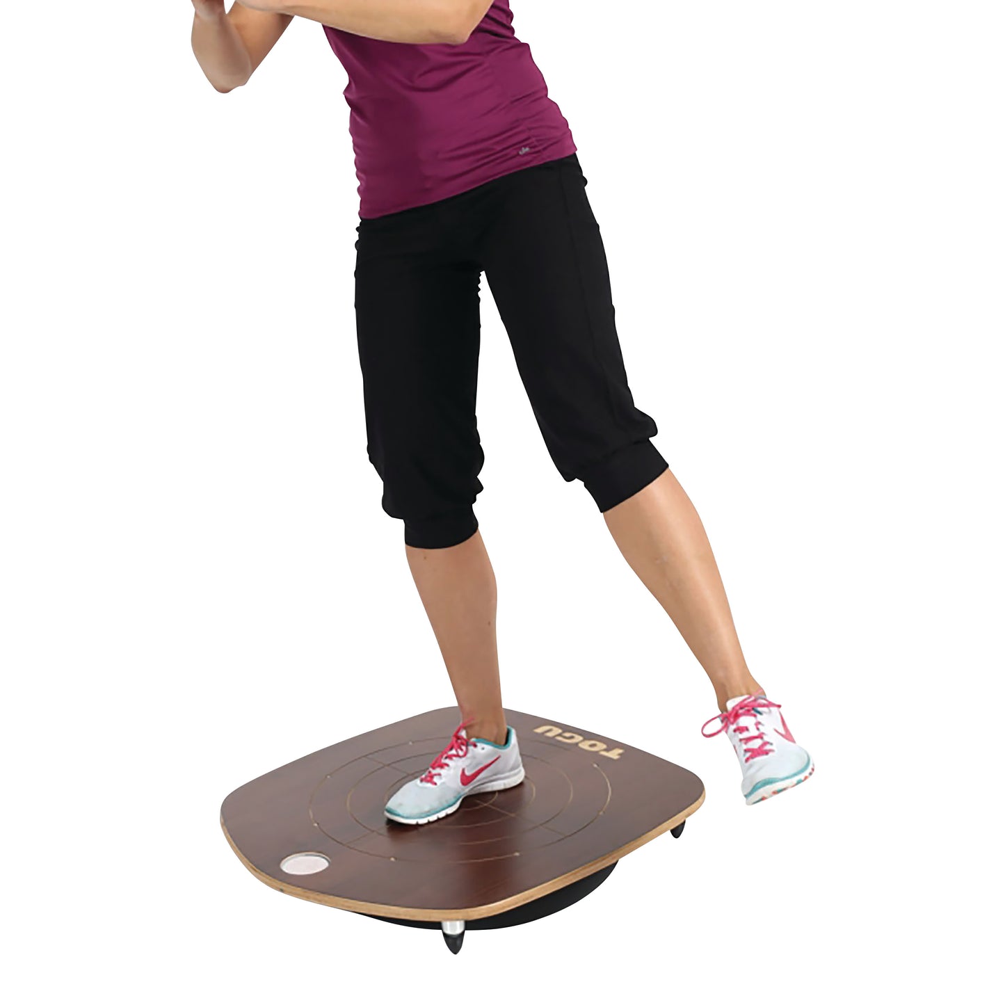 A person balances on a TOGU Posturedo Balance Board, wearing black pants and a purple shirt, one foot on the board and one lifted.