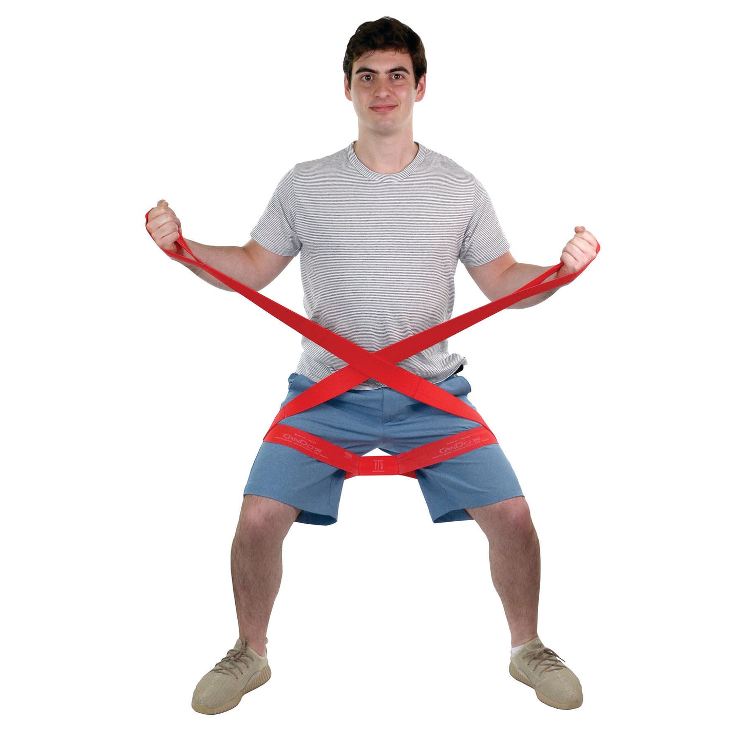 A person demonstrates the CanDo Multi-Grip Exerciser, a red resistance band, while standing in a semi-squat position.