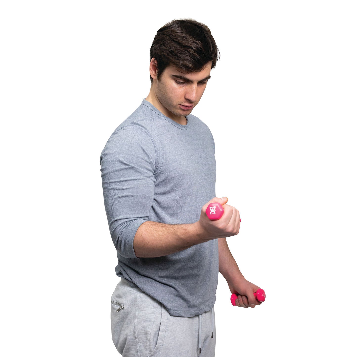 A person in a gray shirt lifts a pink CanDo Vinyl-Coated Dumbbell while looking at it, with another dumbbell in the other hand.
