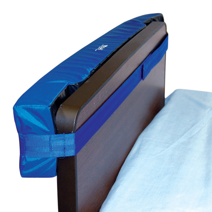 The SkiL-Care Headboard/Wall Protector is a blue padded cover attached to the top edge of a dark wooden headboard for protection.