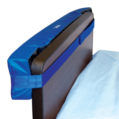 The SkiL-Care Headboard/Wall Protector is a blue padded cover attached to the top edge of a dark wooden headboard for protection.
