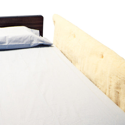 A SkiL-Care Synthetic Sheepskin Bed Rail Pad is attached to a bed rail, next to a pillow and bedsheet.