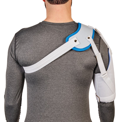 A person wears an AliMed Hemi-Shoulder Sling over a gray shirt, providing shoulder support with wide straps and padding.