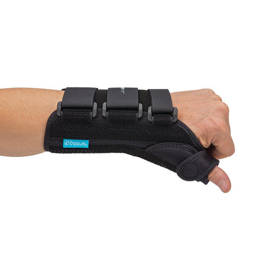 A forearm wearing an �ssur Formfit Thumb Spica Splint. It's black with adjustable straps, supporting the wrist and thumb.