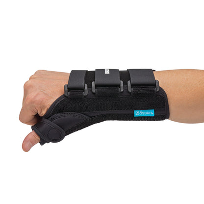 A hand wearing the �ssur Formfit Thumb Spica Splint, a black wrist brace with thumb support and adjustable straps.