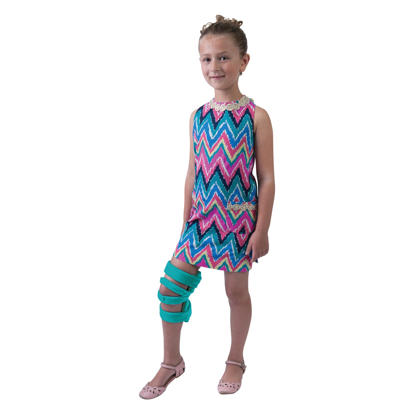 A young girl wears a Comfy Splints Pediatric Goniometer Knee Orthosis. She is dressed in a colorful, zigzag-patterned dress.
