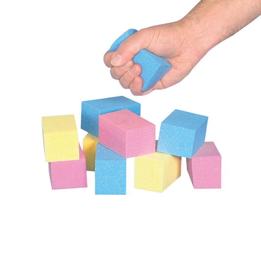 A hand squeezes a blue cube from the AliMed T-Foam Visco Cube Set, with additional blue, pink, and yellow cubes stacked below.