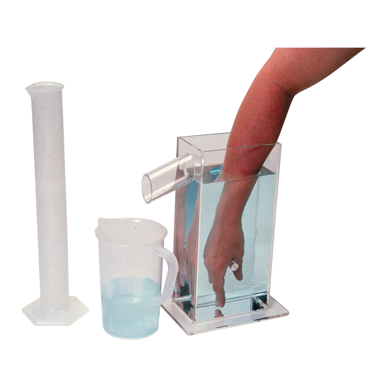 A hand is submerged in a Baseline Volumeter Set filled with water, with a graduated cylinder and a measuring jug beside it.