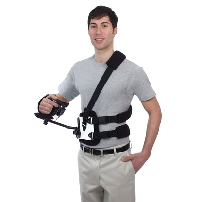 A person wears the Trulife Gunslinger II orthosis, a shoulder and arm brace with straps, over a gray shirt and khaki pants.