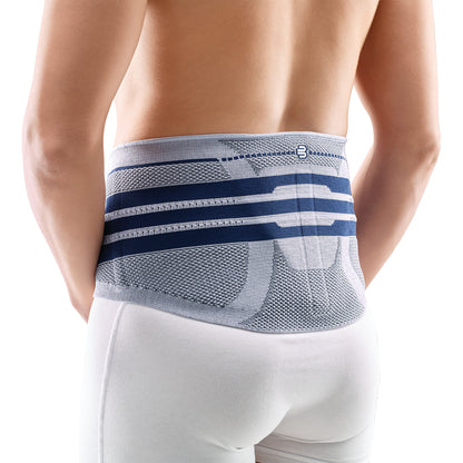 Person wearing the Bauerfeind LumboTrain Back Support, a blue and gray supportive garment, over white pants on their lower back.